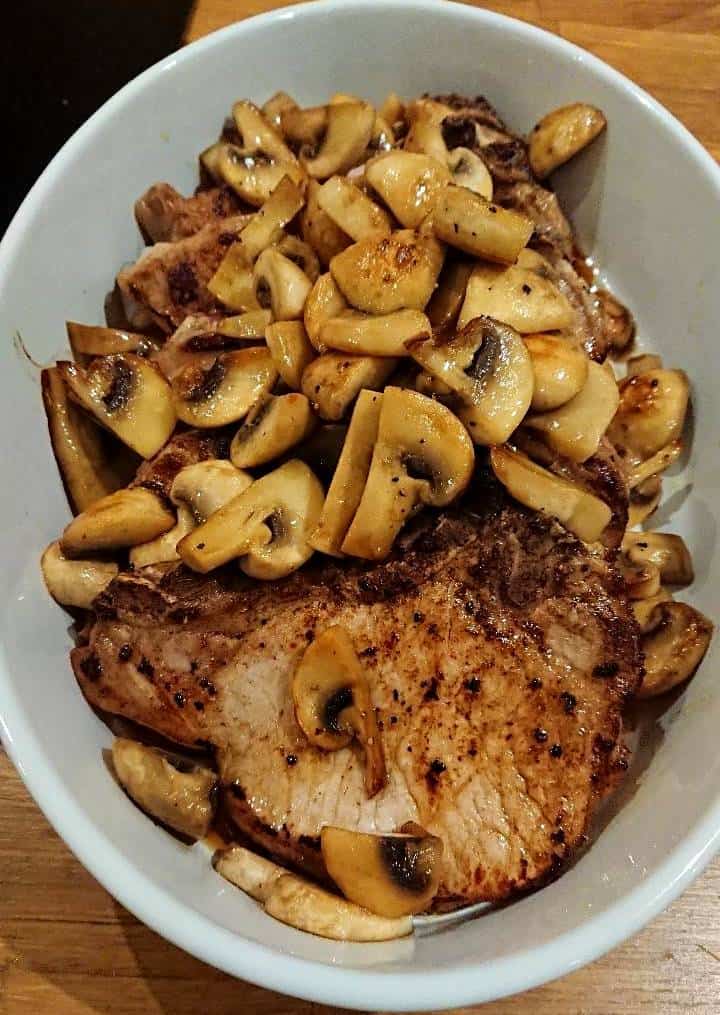 En skål med stekt fläskkött toppat med skivade champinjoner.
